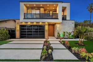 Modern two-story house with a landscaped front yard, featuring large windows and contemporary design, at dusk.